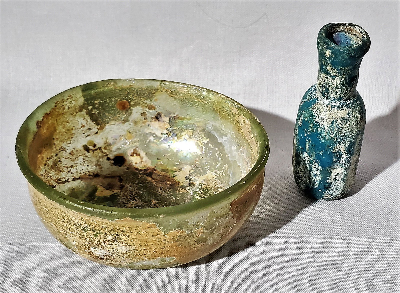 Two Pieces of Roman Glass: Two Roman glass articles. One small bowl and the other a blue glass vial, 1 1/4 in. by 2 3/4 in. diameter for the bowl and 1 1/4 in. high for the glass vial, 1st Century AD