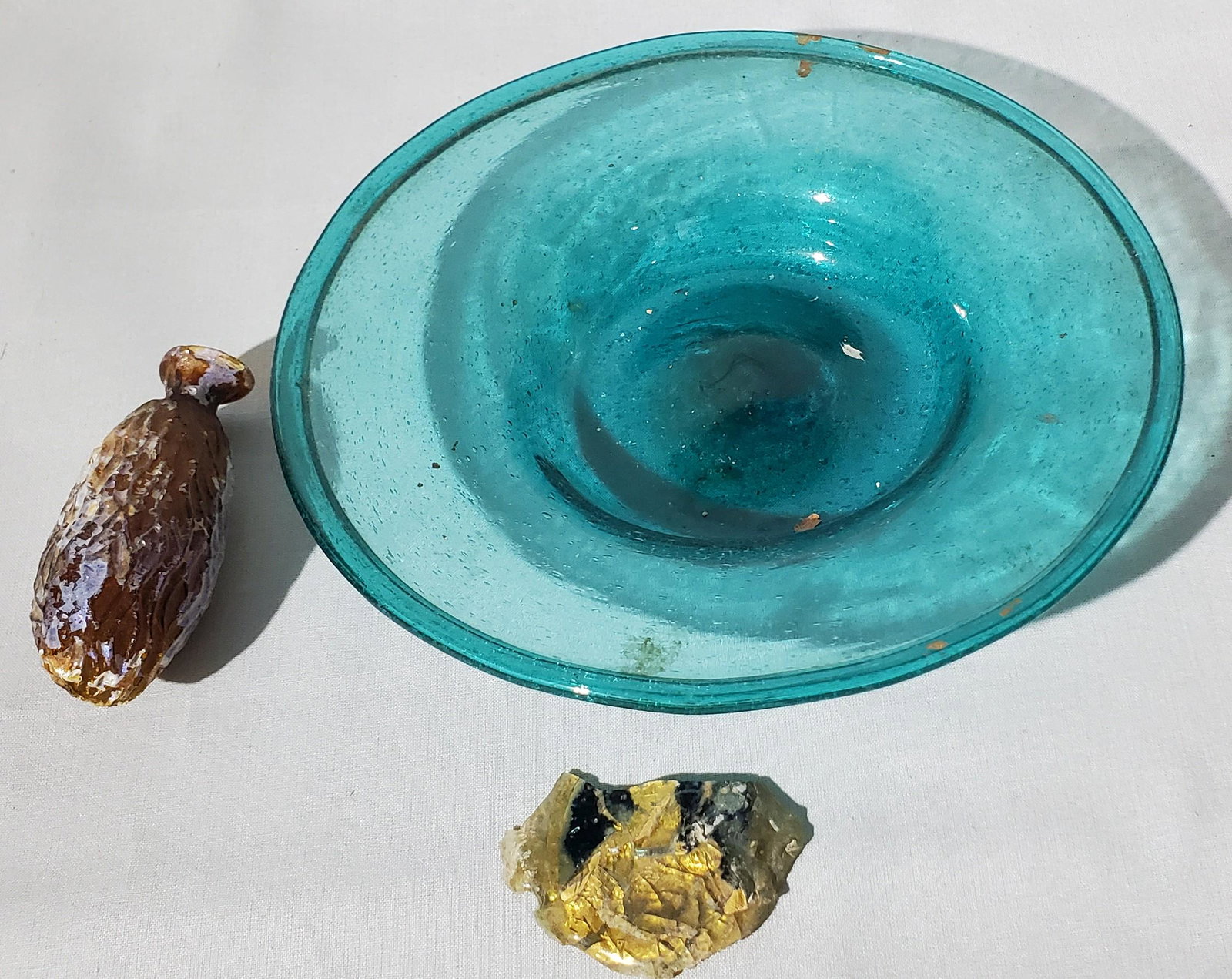 Roman/Byzantine Glass Plate: A Roman or late Byzantine glass plate with traces of iridescence together with a late Roman portrait encased in glass with gold leaf, circa 4th/5th Century AD and a rare perfume flask with a shape of