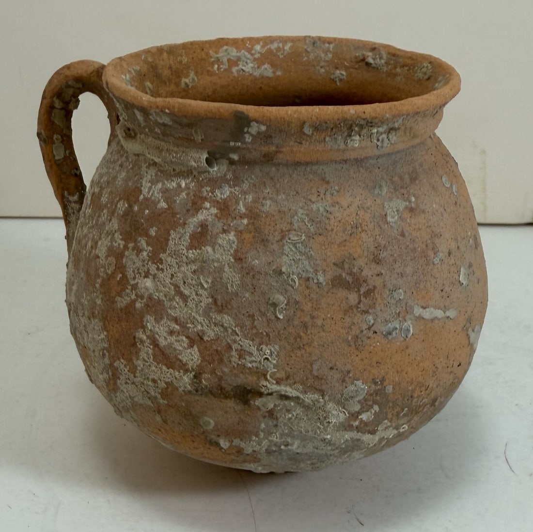 Roman Globular Terracotta Drinking Vessel, 1st to 2nd C AD: With surface accretions as expected with age. Height: 3 1/4 inches, Width: 3 7/8 inches including handle. Weight: 4.2 oz.