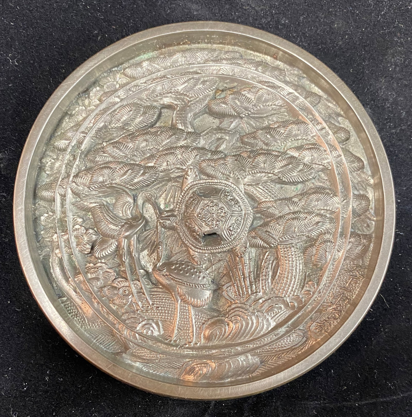 Chinese Bronze Mirror with Pine and Crane: Auspicious imagery with decoration cast in relief. Diameter: 4 1/2 inches, Depth: 3/8 inch. Weight: 1.4 oz. This item is at our New York location.
