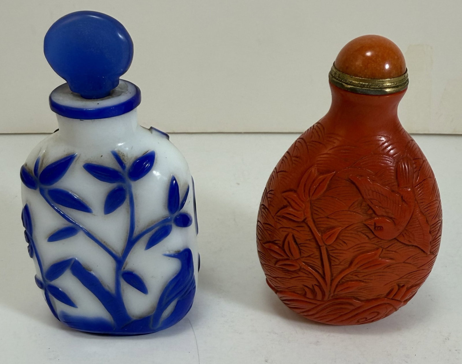 Two Chinese Glass Snuff or Scent Bottles: One blue on white overlay, the other coral color glass. Height: 3 x 2 x 1 inch and 3 1/8 x 2 1/8 x 1 1/4 inches, not including stopper. Weight: 9.5 oz. total. This item is at our New York location.