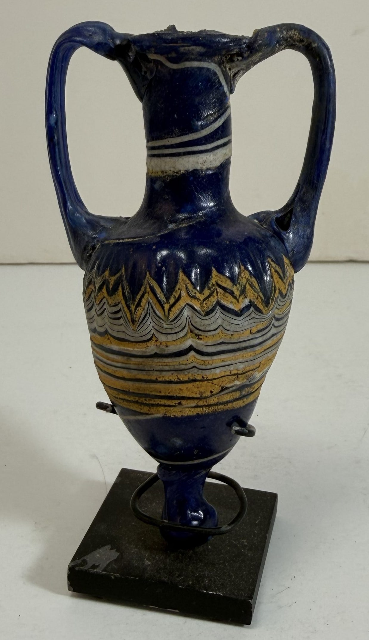 Ancient Greek Blue Glass Amphora Amphoriskos with Yellow and White Decoration: With a stand. Height: the glass 4 1/4 x 2 1/4 x 1 5/8 inches. Weight: 2.6 oz., with the base 5.2 oz.