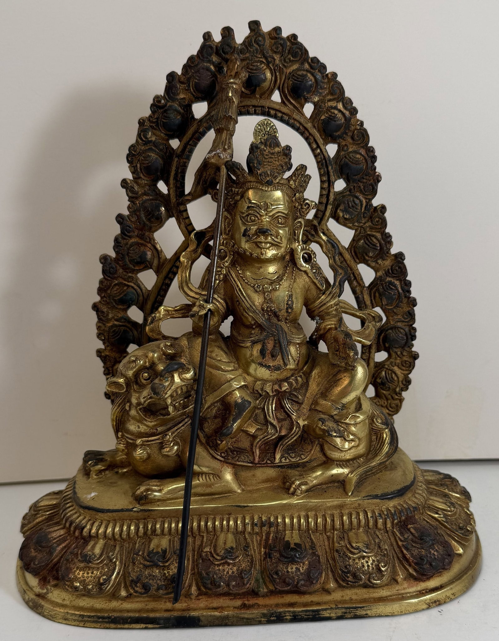 Sino Tibetan Gilt Bronze Figure of Jambhala: The figure seated on a tiger, and holding a staff, some rubbing to the gilding. Height: 8 1/4 inches, Width: 7 1/4 inches, Depth: 3 1/2 inches. Weight: 3 lbs. 2 oz. This item is at our New York locati