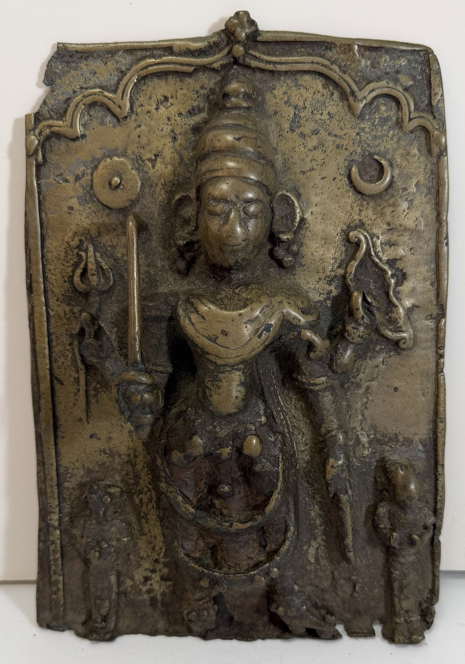 Early Indian Brass Plaque with Shiva Cast in Relief: The figure with four arms, holding a sword, a bow, and a trident. Some losses to the metal along the edges of the plaque, some rubbing and wear to the surface. The plaque 8 by 5 1/2 inches, Depth: 1 1