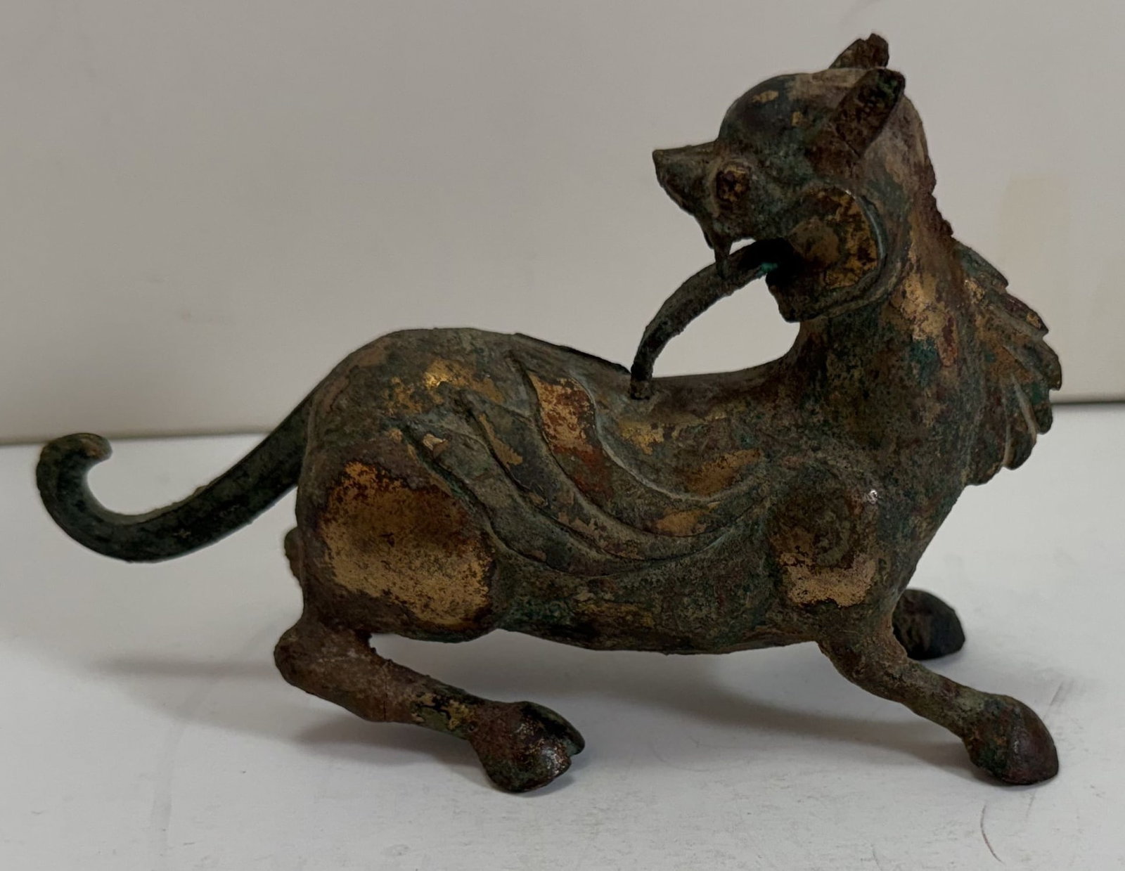 Chinese Gilt Metal Figure of a Qilin: The qilin sculpted with hooded feet and a long tongue with remnants of gilding. Length: 6 inches, Height: 3 1/2 inches, Width: 2 1/2 inches. Weight: 12 oz. This item is at our New York location.