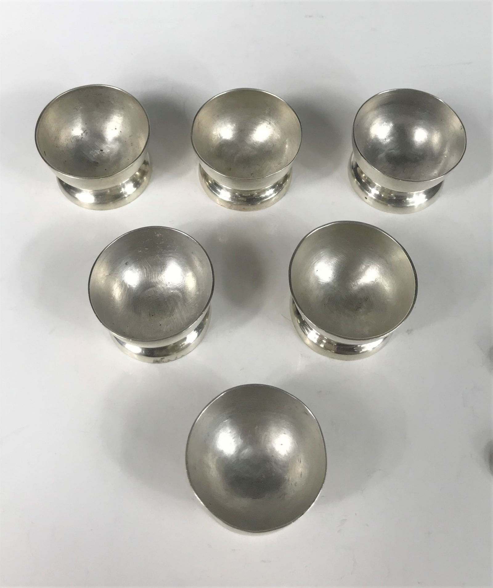 William Spratling (1901-1967) - Six Footed Silver Salt Cellars and Spoons, c. 1940: A set of six sterling footed salt cellars and spoons by William Spratling. Made in Mexico, 1940-1946 hallmarks. Dimensions: Cellars - 1 1/4 in. tall x 1 5/8 in. diameter, Spoons - 2 1/2 in. long, weig