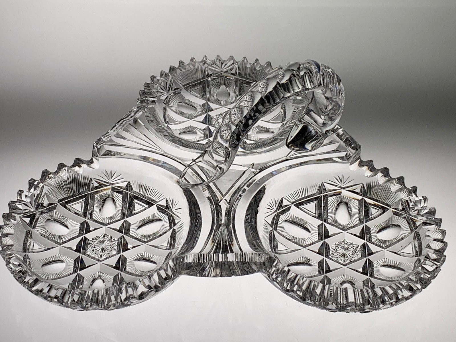 Unique Pairpoint Handled 3 Compartment Cut Glass Dish: This unique American Brilliant cut glass dish has three compartments with an attached handle. It was cut by Pairpoint in the Nevada pattern. Circa 1900. Approx. dimensions: 11" long, 4" high at handle