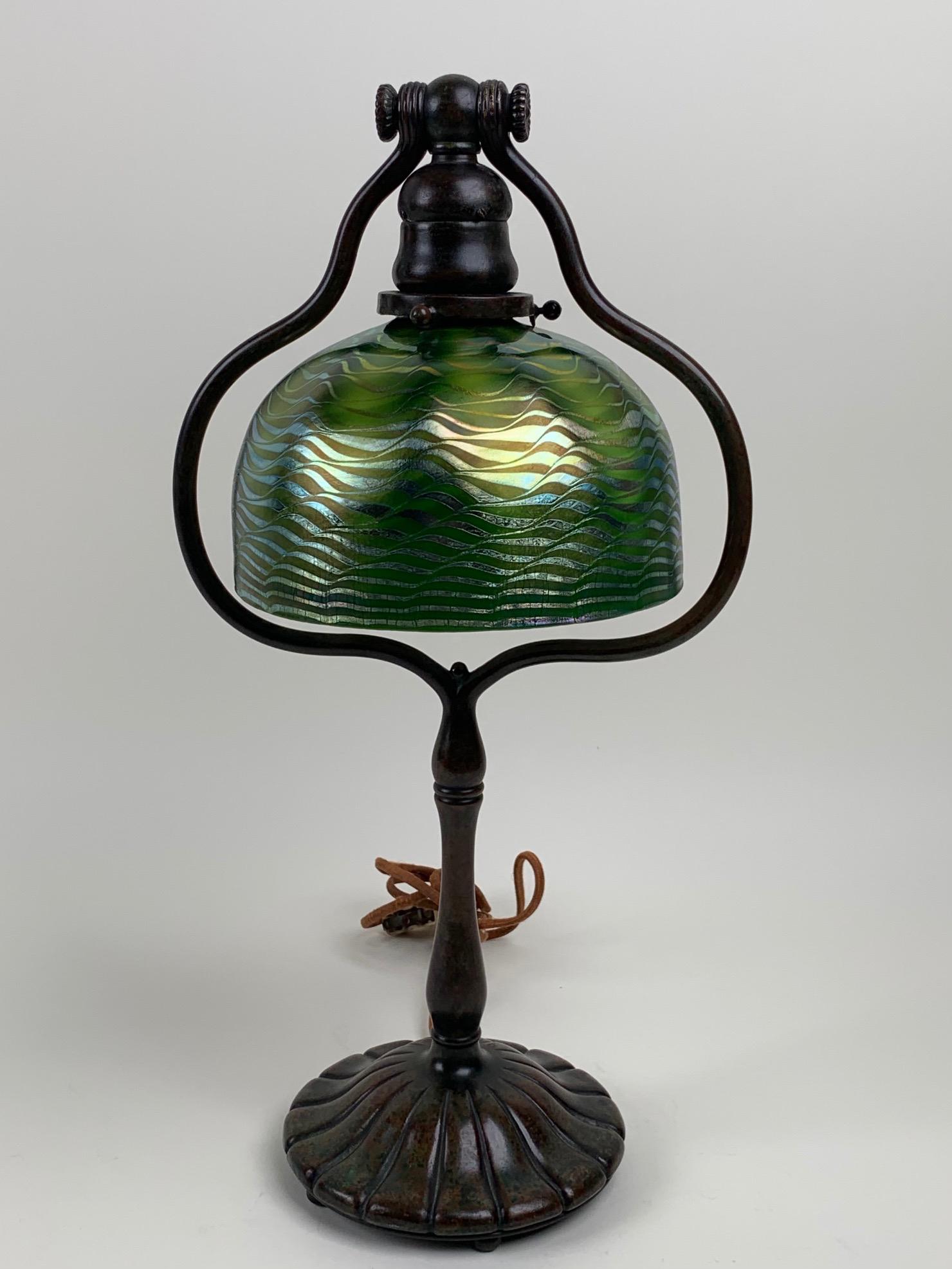 Tiffany Studios Favrile Glass Bell Lamp: Bronze bell desk lamp with favrile glass shade in iridescent green with a wave design. Bronze base is signed Tiffany Studios New York. It has a beautiful aged patina. Signed on base Tiffany Studios an