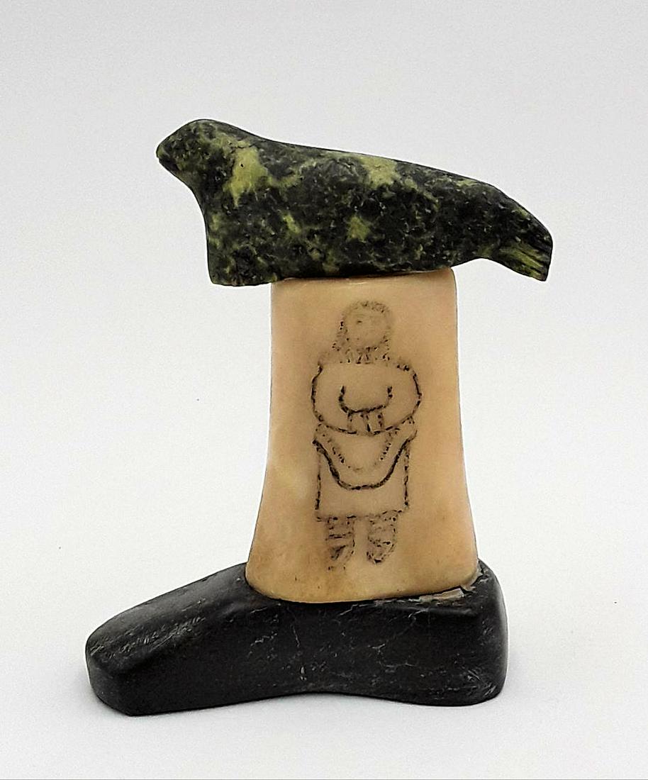 INUIT SEAL CARVING: Cape Dorset / Frobisher Bay, circa 1960s Carved stone seal resting atop a bone having a male figure on one side and a female figure on the other set on a stone base. 5.75" h x 4.5"w x 2"d
