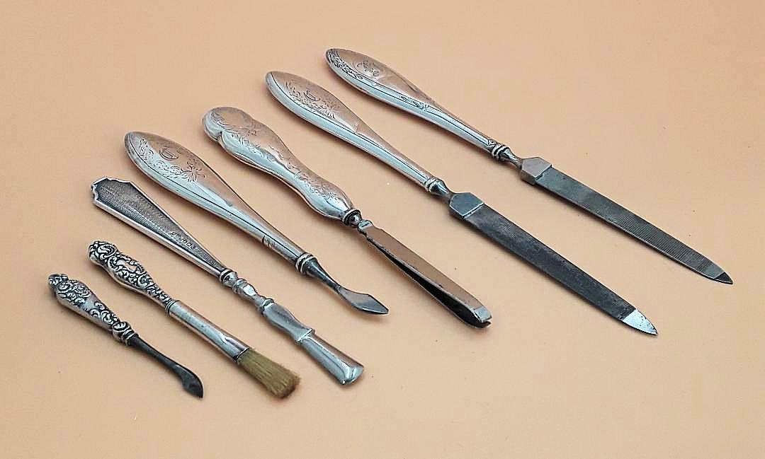 SILVER DRESSER MANICURE GROUPING: Seven antique silver-handled pieces including two nail files; three cuticle pushers; tweezers; and a small brush. Ranging from 7.5" to 2.5" long