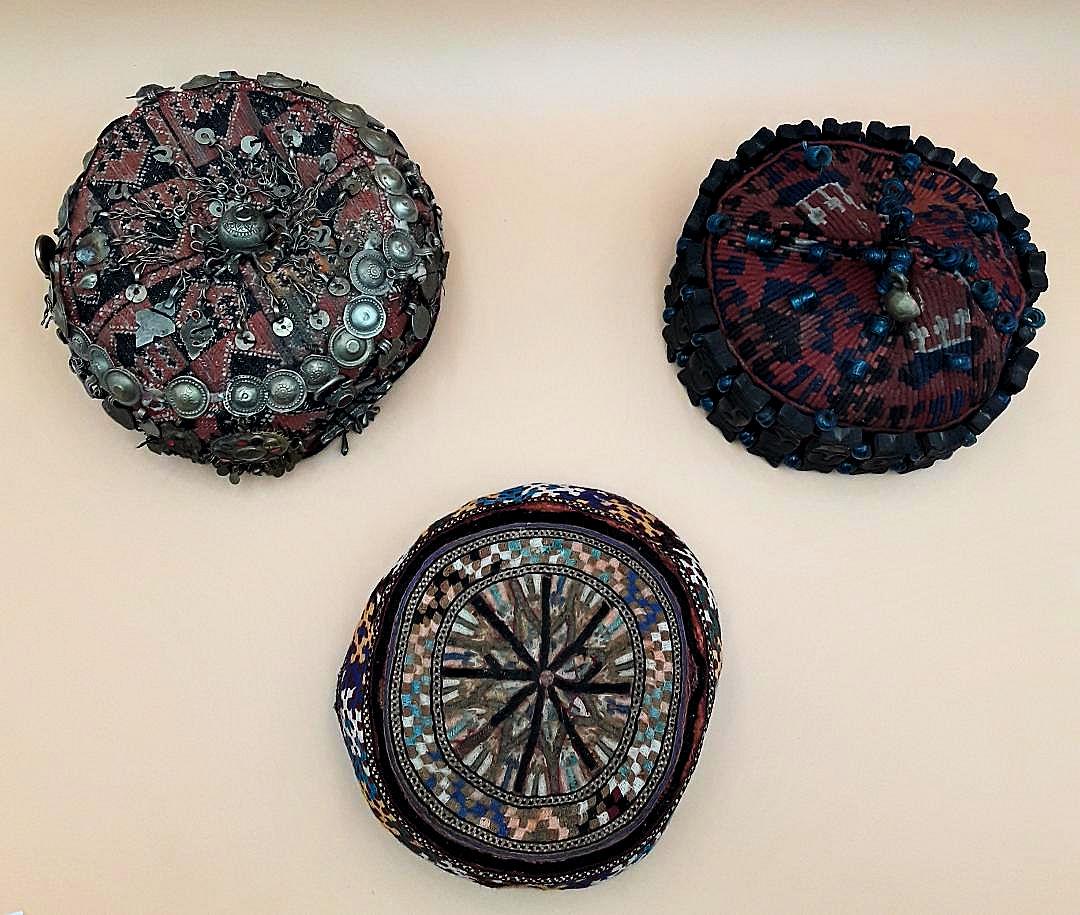 THREE ANTIQUE AFGHAN TRIBAL HATS: Three antique tribal caps Afghan or possibly Tibetan. One is richly decorated with metal chains, ornaments and beads, another is covered in blue glass beads, a bell and carved wooden faces surrounding