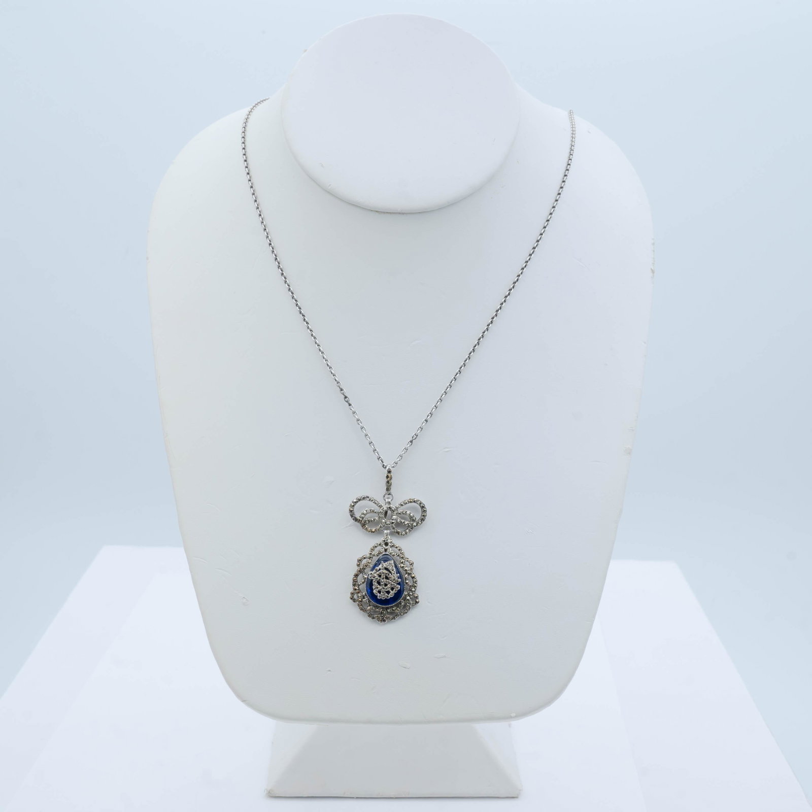 VICTORIAN SILVER AND MARCASITE NECKLACE: Delicate 19th century silver, blue glass and marcasite pendant suspended from a silver chain. The tear drop pendant is suspended from a bow and bail set with marcasites and is set in a pretty pierced 