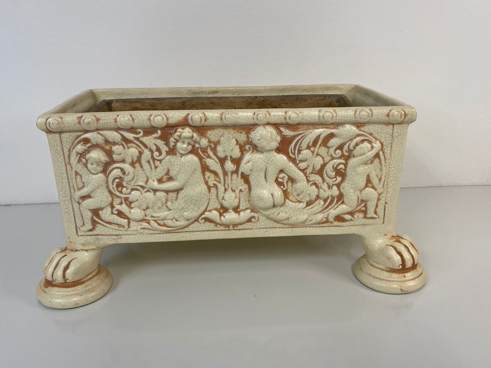 Weller Pottery Ivory: This window box in the ivory glaze has 4 clawed feet and lots of cherubs and includes the original pottery insert. Measures 7 1/4" tall and 15" long