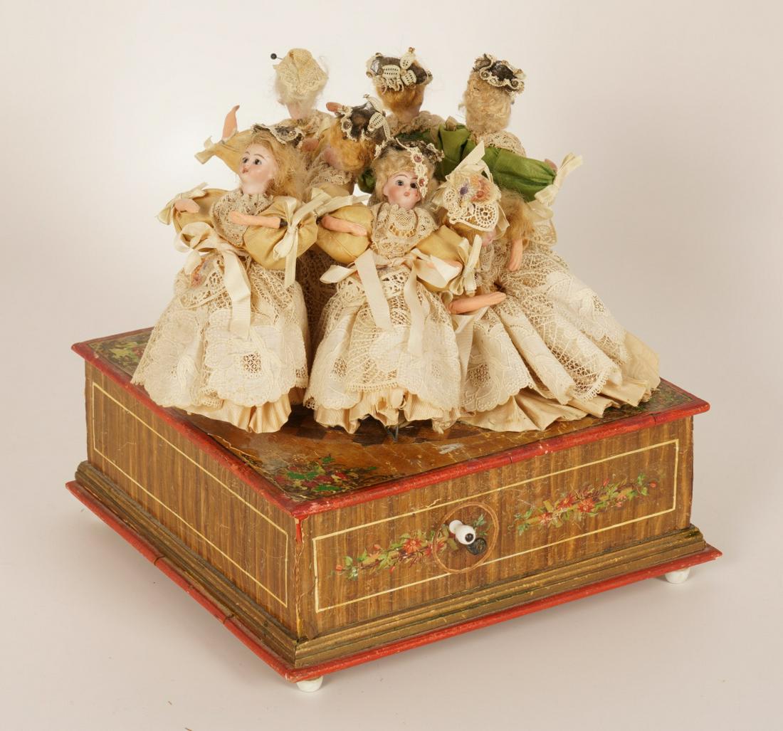 Manivelle German Victorian Automaton Dolls: 7 Closed mouth porcelain dolls with glass eyes and period laced costumes, attached to a center carousel, resting on a painted paper decorated vase with windup crank