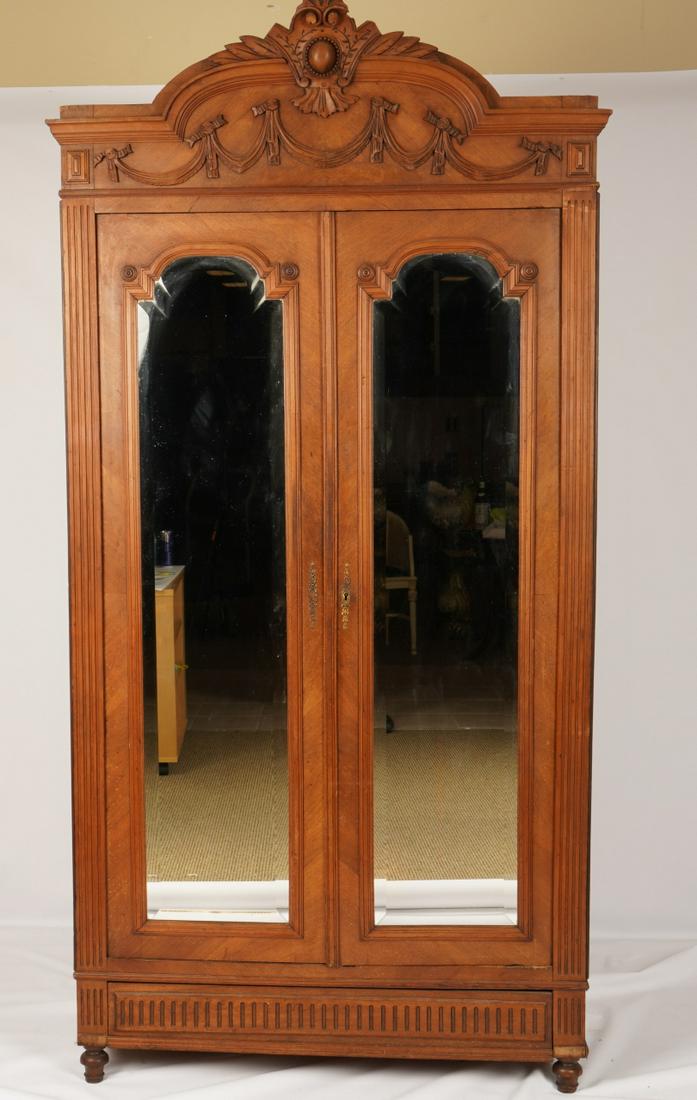 Louis XVI Style Mirrored Door Armoire: Applied carved cornice over two beveled glass doors revealing interior fitted with shelves and secret drawer above additional lower secret drawer. Walnut or mahogany veneer.