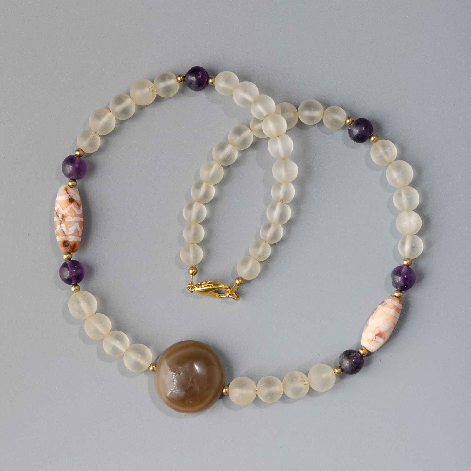 Indo-Tibetan Antique Necklace – Magic Eye and Mixed Gemstone Beads: A unique antique Indo-Tibetan necklace composed of mixed stone beads, including crystal, amethyst, etched carnelian, and a striking magic eye bead at the center.Length: 20 inWeight: 57 g