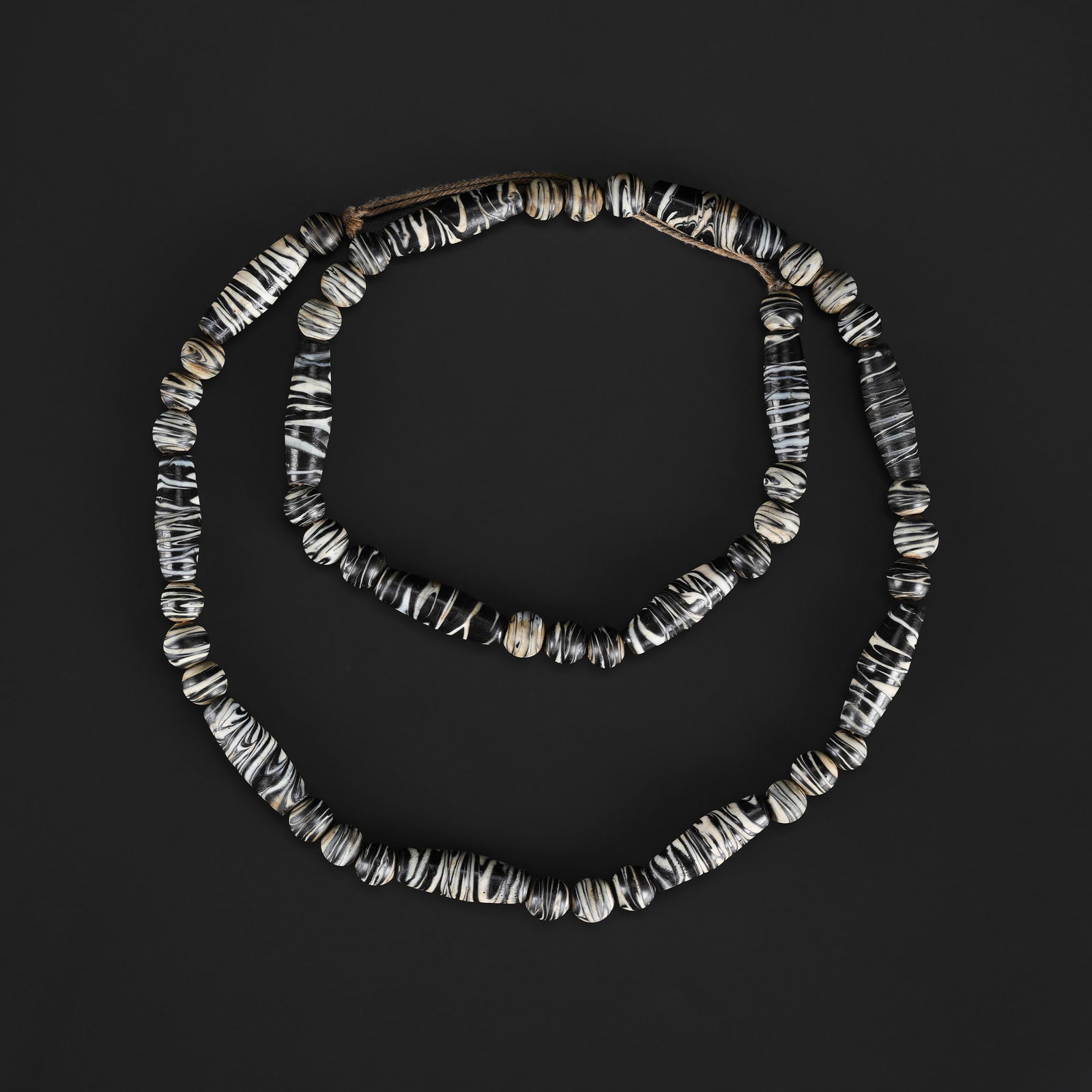 An Antique Banded Black and White Barrel Glass Bead Necklace: An antique necklace composed of banded black and white barrel-shaped glass beads, exhibiting bold contrast and surface wear consistent with age and use. Length: 30in Total Weight: 108gram