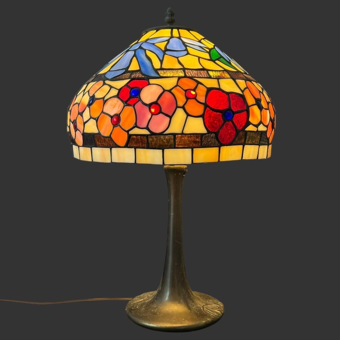 Vintage Tiffany Style Metal & Leaded Glass Lamp: Vintage Tiffany Style Metal & Leaded Glass Lamp. This lamp is in working condition. Approximate dimensions with shade (in): 22.25 (to the top of the finial) x 13.75 x 13.75.. Buyer pays shipping cost.