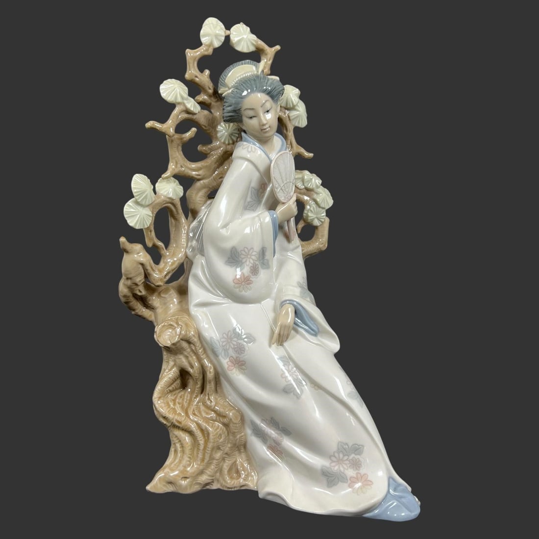 Lladro Spain Porcelain 'Geisha' Figurine: Lladro Spain Porcelain 'Geisha' Figurine. It was sculpted by Vincente Martinez, features a serene geisha seated gracefully on a tree branch, adorned in a beautifully detailed kimono with intricate flo
