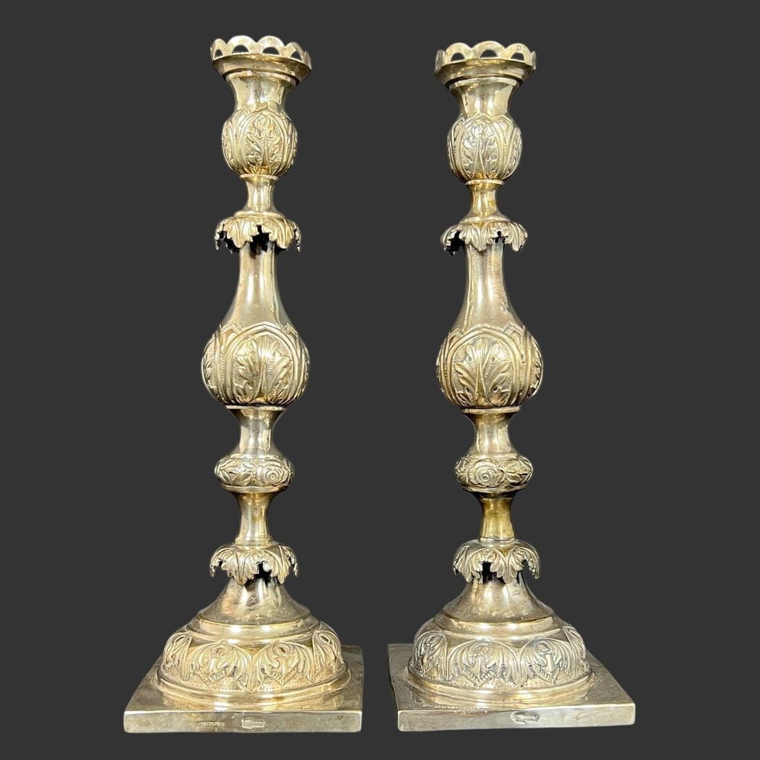 Pair of Ornate Russian 84 Silver Candlesticks: These candlesticks have a detailed design with a square base, an ornate baluster-shaped body, and decorative elements such as acanthus leaves and foliage. This style is described as Baroque or Revival