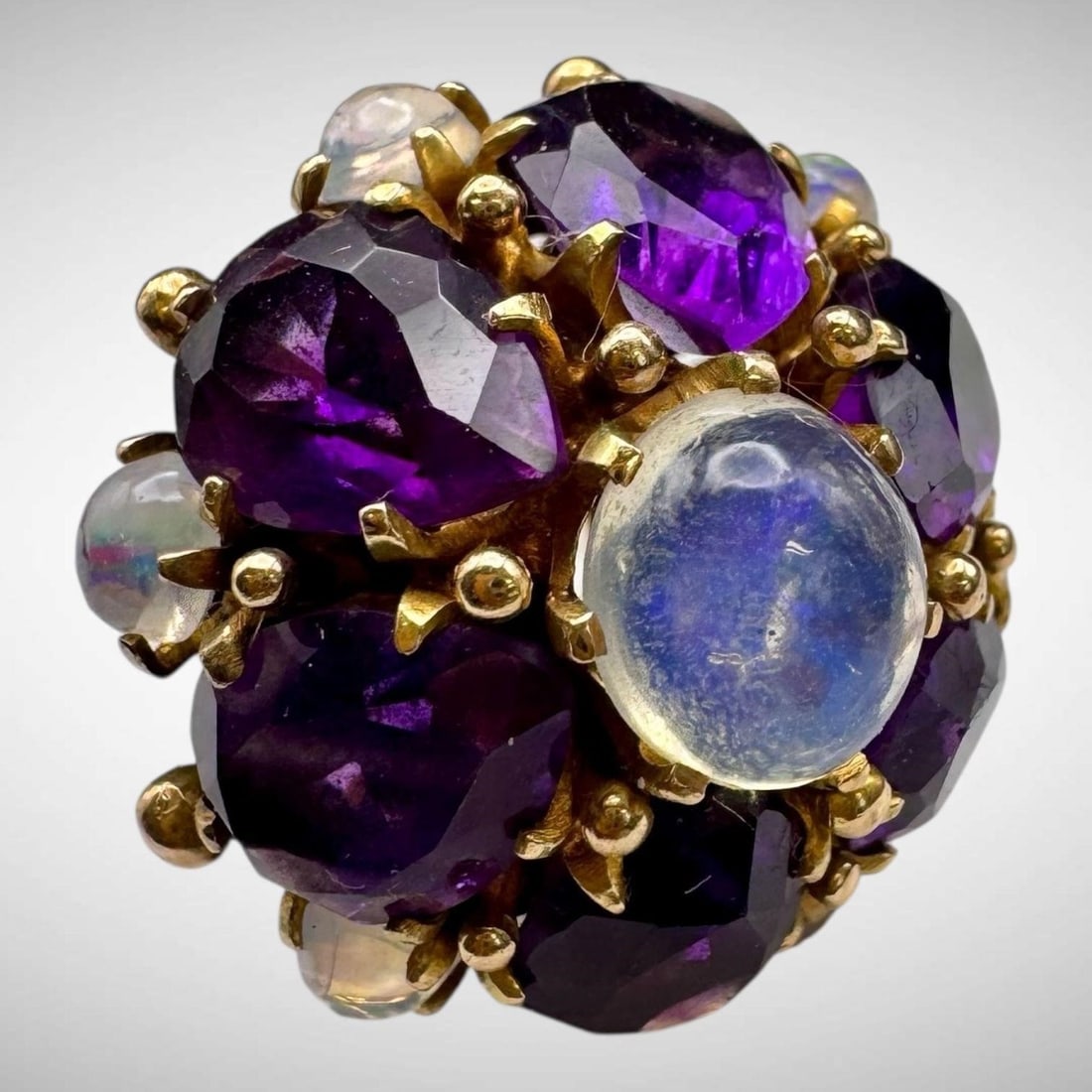 Vintage 14K Amethyst Moonstone Dome Ring: Dimensional floral design ring featuring cluster of marquise shape faceted amethysts and moonstones cabochons. Hallmarked 14K. Ring size 7.5. Face of the ring measures: 1", rises 0.75" above the finge