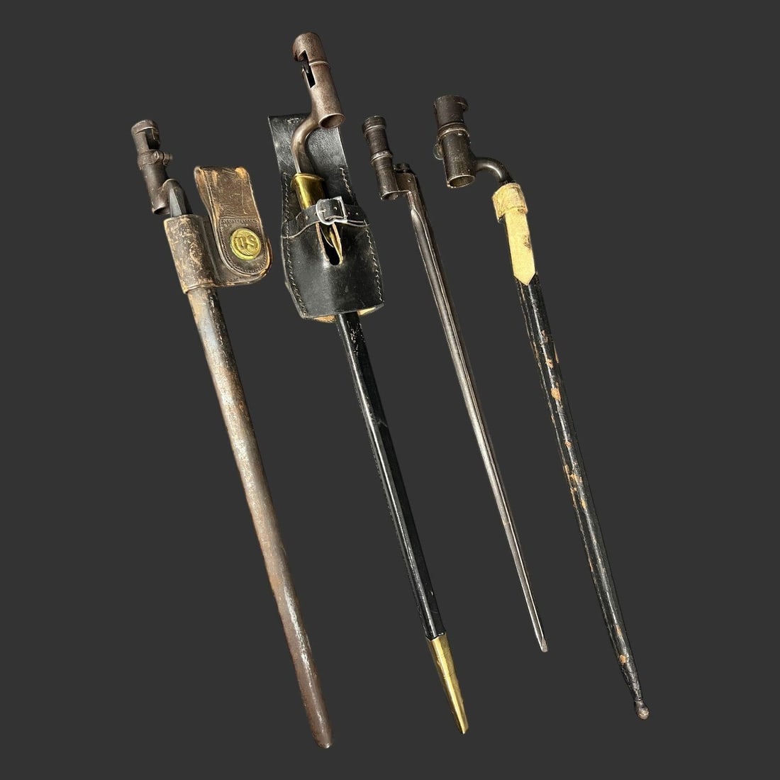 (4) U.S. & European Socket Bayonets with Scabbards: This lot offers a compelling quartet of antique socket bayonets representing both American and European 19th-century military arms. The group includes one U.S.-marked example clearly stamped "US" on t