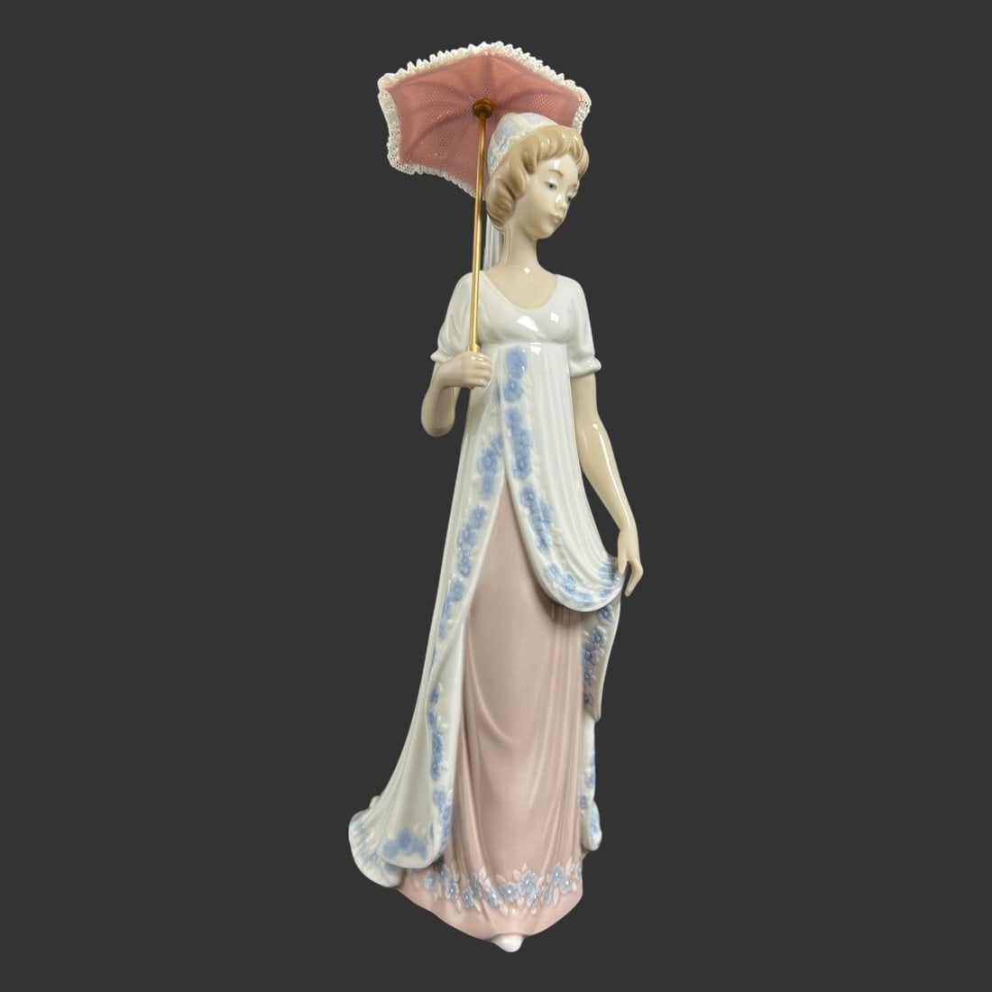 Lladro Spain Porcelain #5322 'Viennese Lady': This elegant glazed porcelain figurine by Lladro depicts a refined young woman in a flowing pastel gown, delicately holding a parasol. The figure is rendered in Lladro's signature soft palette, with a