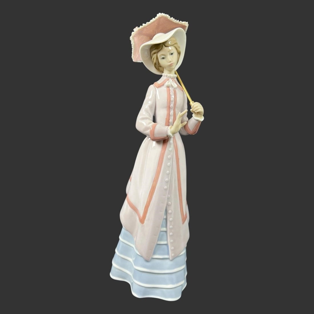 Lladro Spain Porcelain #5321 'Parisian Lady': This elegant Lladro porcelain figurine depicts a refined young woman in flowing pastel attire, gracefully holding a parasol. Rendered in the soft, romantic palette for which Lladro is known, the figur