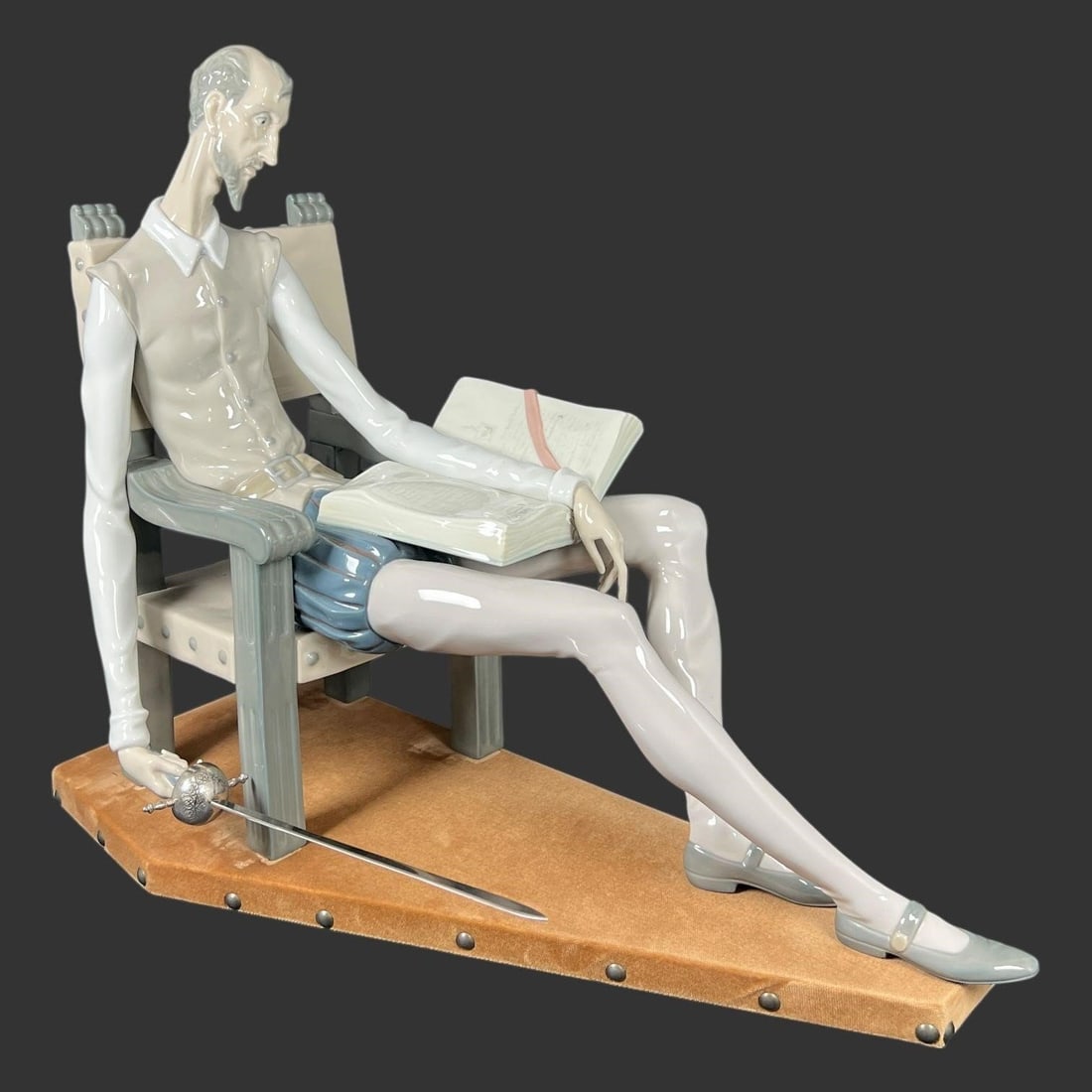 Lladro Spain Porcelain Figurine #1030 Don Quixote: This finely detailed Lladro porcelain figurine depicts Don Quixote seated in a chair, absorbed in a book, with his sword resting at his side-an evocative scene that captures the literary character's i