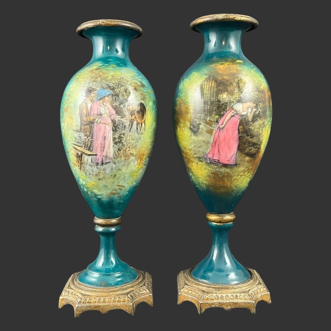 Pair of Antique Hand-Painted Enamel Vases: This elegant, matched pair of antique enamel vases features richly detailed hand-painted pastoral and romantic scenes set against a luminous teal-blue ground, framed by soft golden highlights that glo