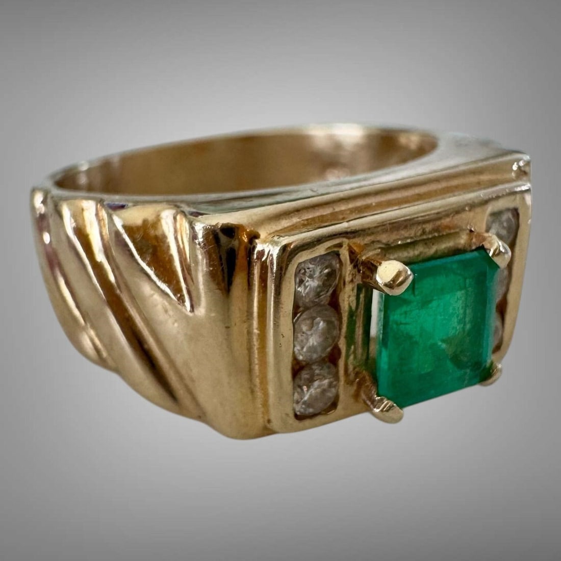 Vintage 14K Gold Emerald Diamond Men's Ring: A striking gentleman's 14K yellow gold ring featuring a square step-cut emerald of vivid green color, flanked by six round brilliant-cut diamonds-three on each side-set within rectangular panels. The