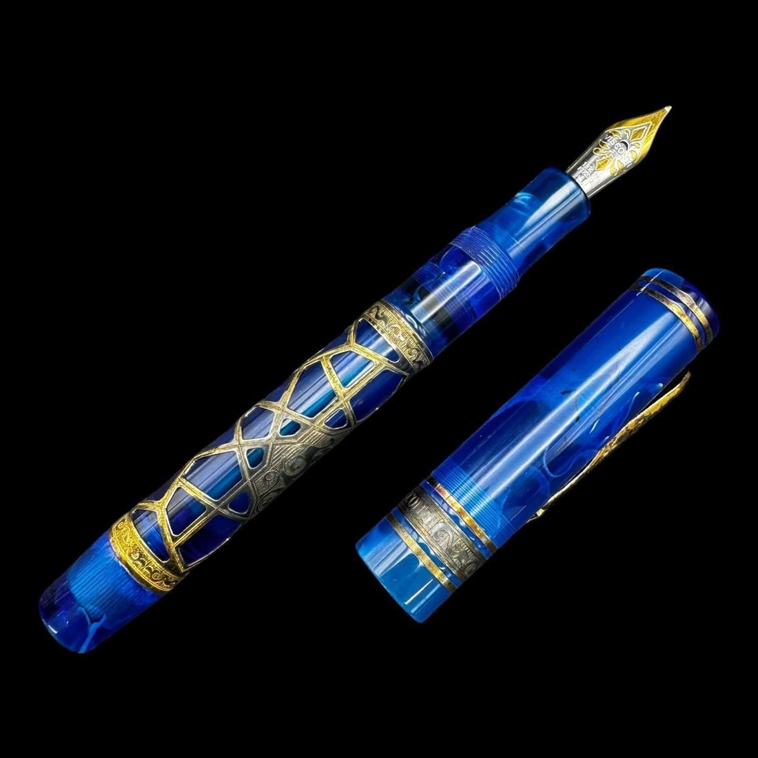 Visconti 18K Blue Celluloid Fountain Pen: Visconti fountain pen featuring a striking translucent blue marbled resin body with ornate gold-tone skeleton overlay and decorative banding. The pen is fitted with a two-tone 18k gold nib marked "VIS