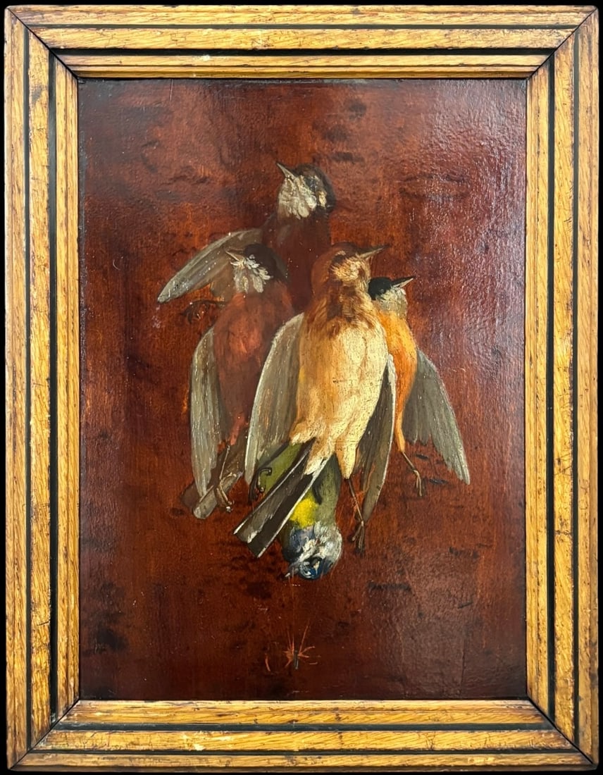 Antique Trompe l’Oeil Still Life Painting of Game Birds on Panel: A charming antique still life painting depicting a hanging group of game birds, executed in a trompe l’oeil style on a dark wood-toned panel. The composition features several birds arranged agai