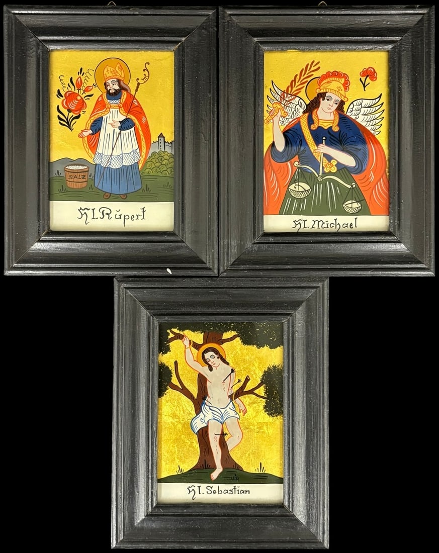 Three Reverse Painted Glass Folk Art Saint Icons Paintings: A decorative set of three framed folk art religious icons depicting St. Michael, St. Sebastian and St. Rupert, each brightly painted in a traditional Central European devotional style with gilt-toned 