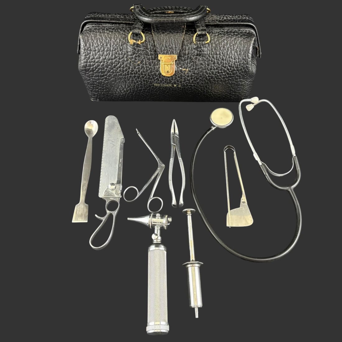 Vintage Lilly Doctor’s Bag with Antique Medical Instruments: A compelling vintage physician’s kit housed in a textured black leather Lilly doctor’s bag, monogrammed “Ted Cohen, M.D.” and featuring a brass clasp. The bag contains an assor