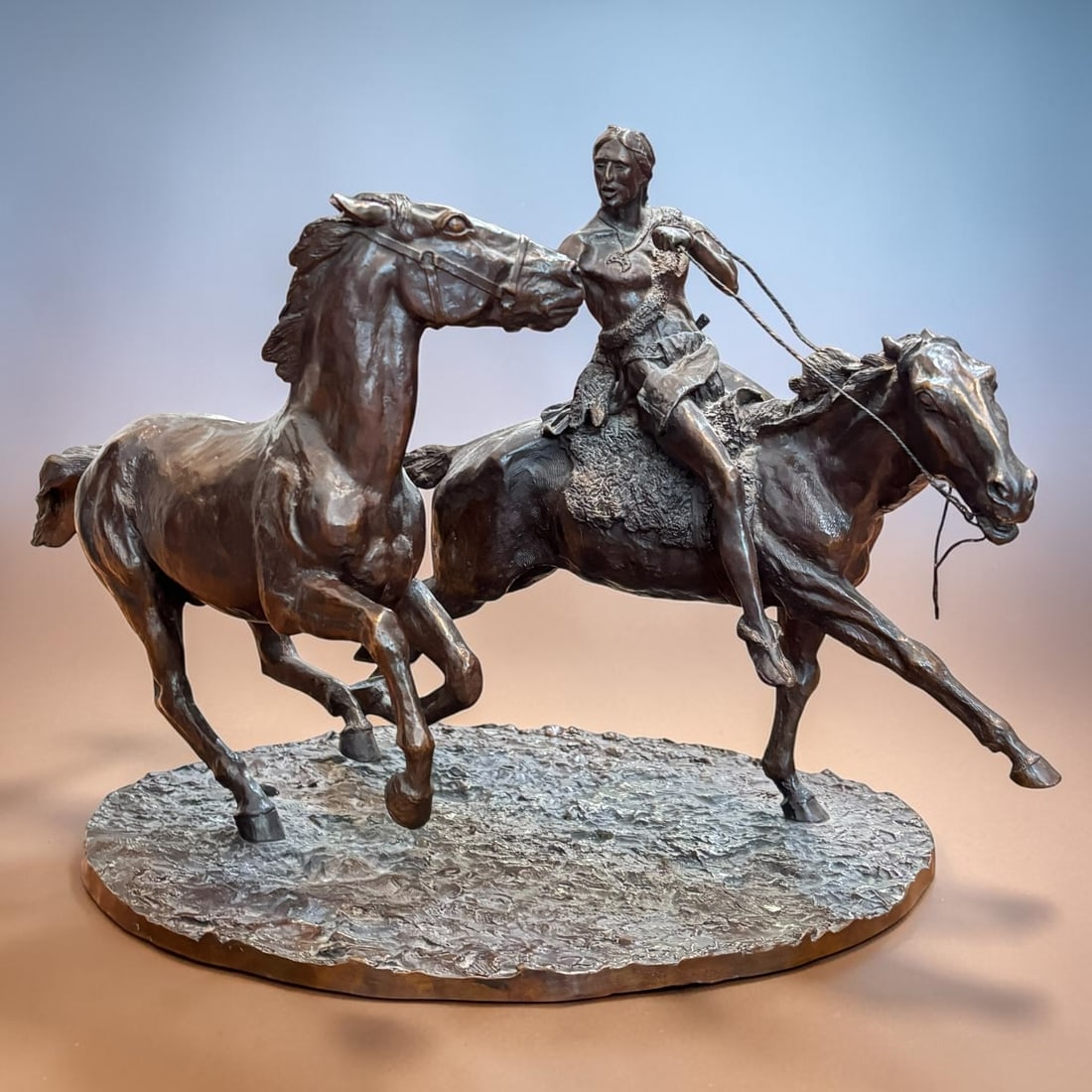 Dante V. De Florio Bronze Native American Rider with Two Horses Sculpture: A dynamic signed bronze sculpture by Dante V. De Florio, depicting a Native American rider mounted bareback while guiding a second horse at full gallop. The work is modeled with strong movement and ex
