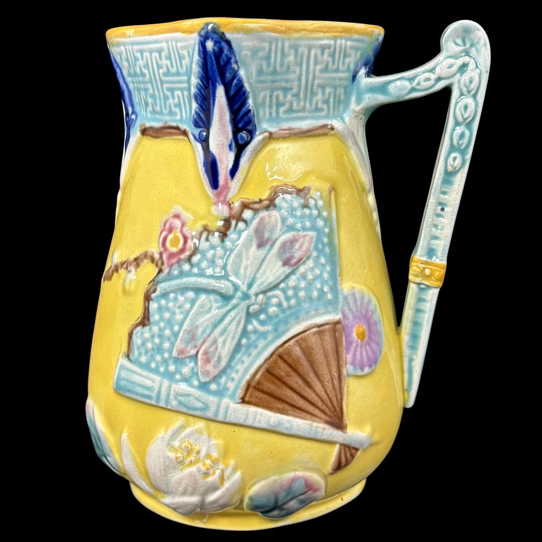 Majolica Japanese Style Pitcher with Fan, Iris & Floral Relief Decoration: A colorful majolica pitcher in Japanese style, decorated with raised relief motifs including a turquoise fan with dragonfly design, molded flowers and leaves, and a bold blue-and-white iris accent ben