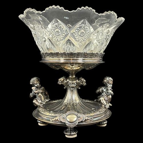 Victorian Silverplate Figural Centerpiece with Cut Glass Bowl: Elaborate silverplate centerpiece featuring a circular footed base decorated with scrolling foliate motifs, applied medallions, and two seated cherub figures holding floral sprigs. The central pedesta