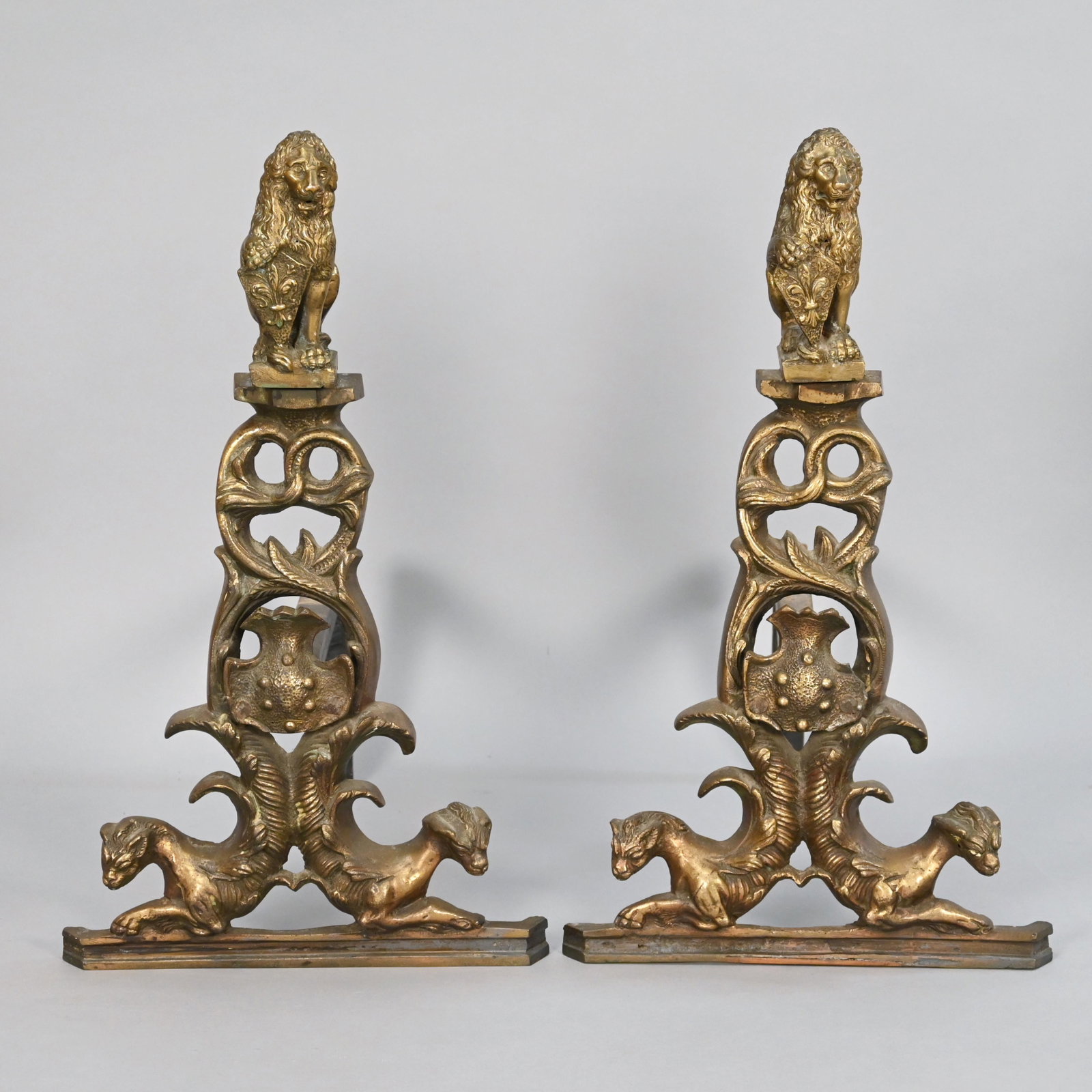 Pair of French Figural Lion Cast Bronze Andirons: Depicting heraldic lions with fleur-de-lis decorated shields above foliate openwork, raised on cat form bases. H: 21.75 in., W: 12.5 in., D: 18 in.