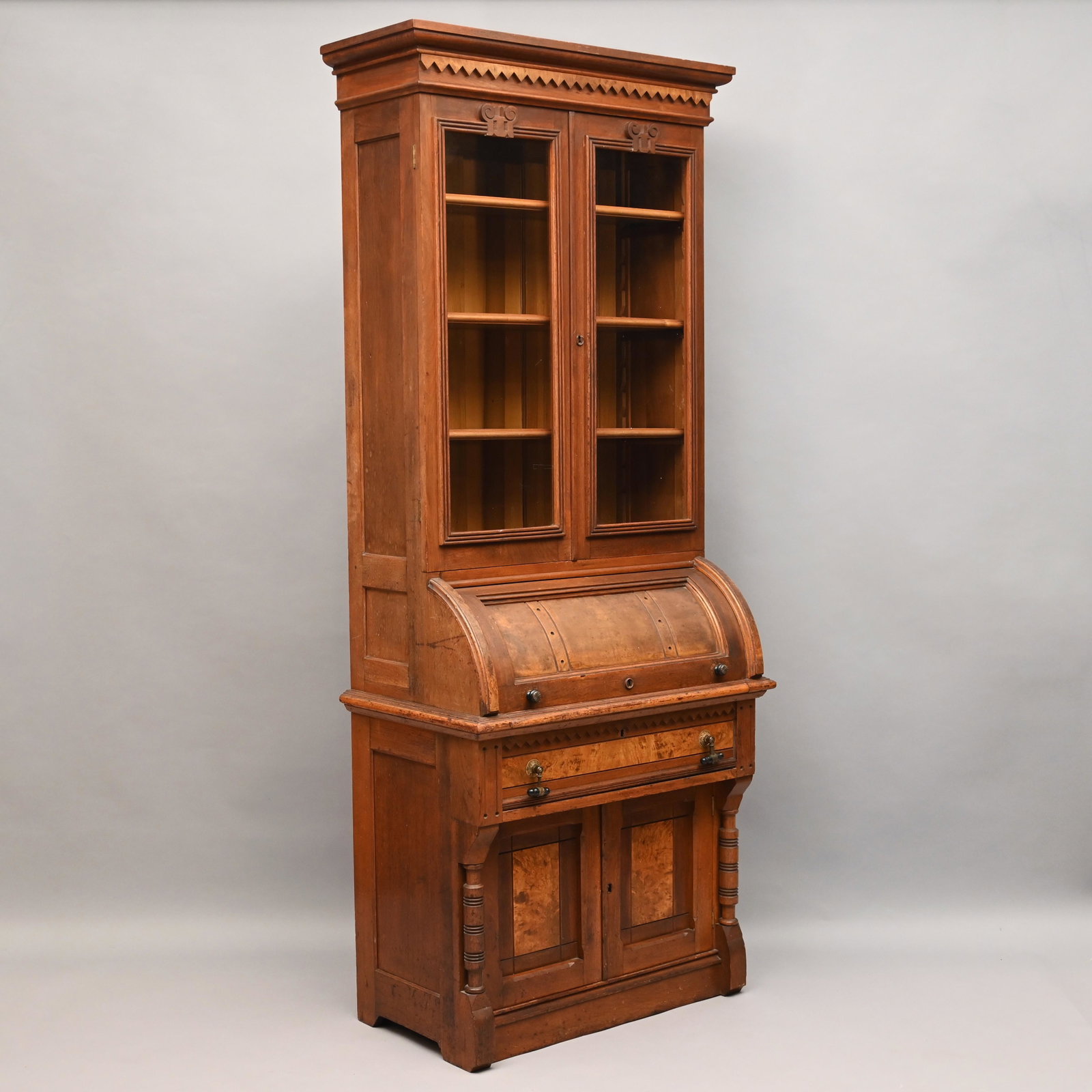 Renaissance Revival Walnut Cylinder Secretary: In two parts: The upper section with molded sawtooth decorated cornice above two doors opening to an adjustable shelved interior, over a quarter round cylinder, opening to a fitted interior. The lower