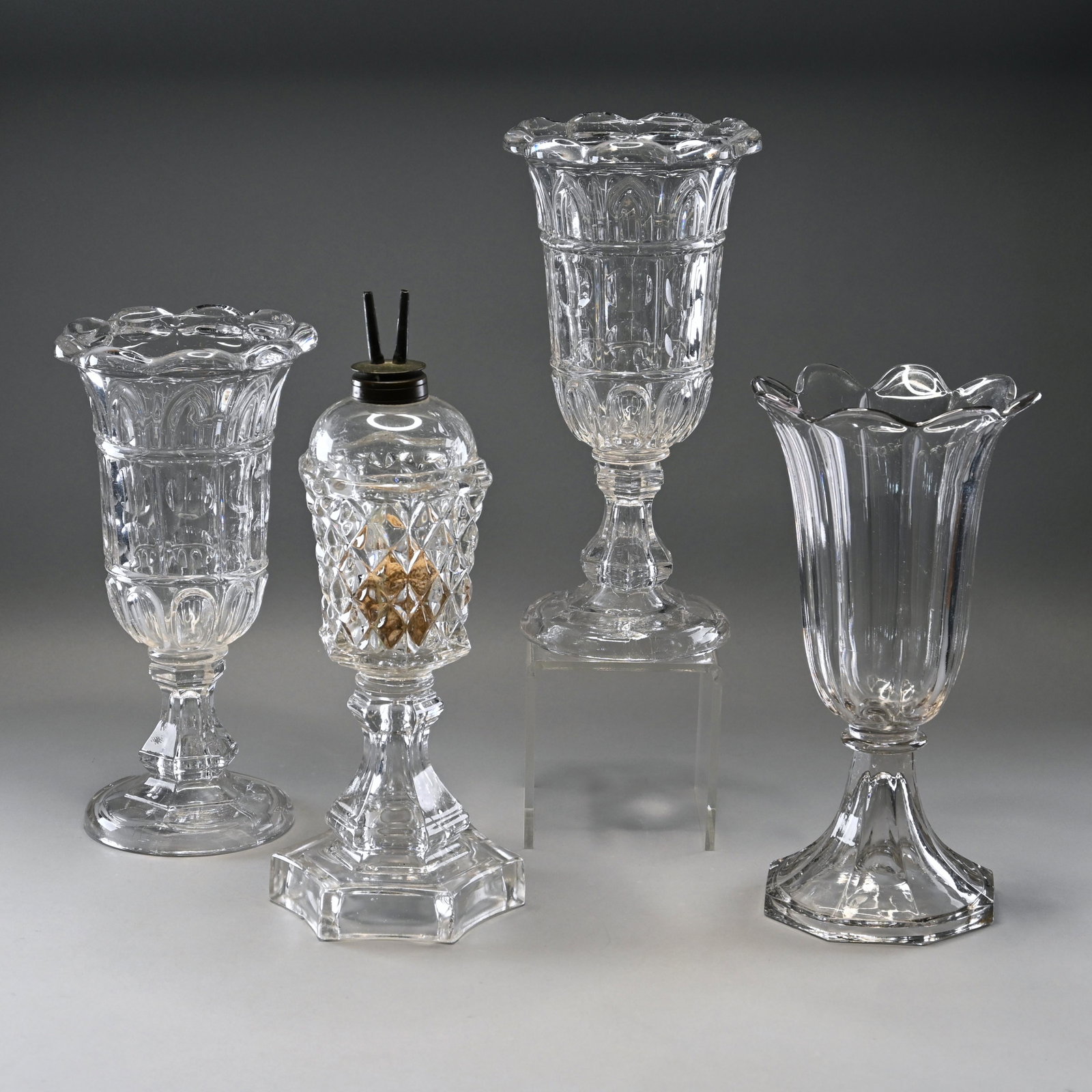 Four Sandwich Colorless Glass Objects: A whale oil lamp together with a pair of gothic arch, printie panel and loop celery vases and a tulip vase. H: 12 in., W: 4 in., D: 5 in. (first)