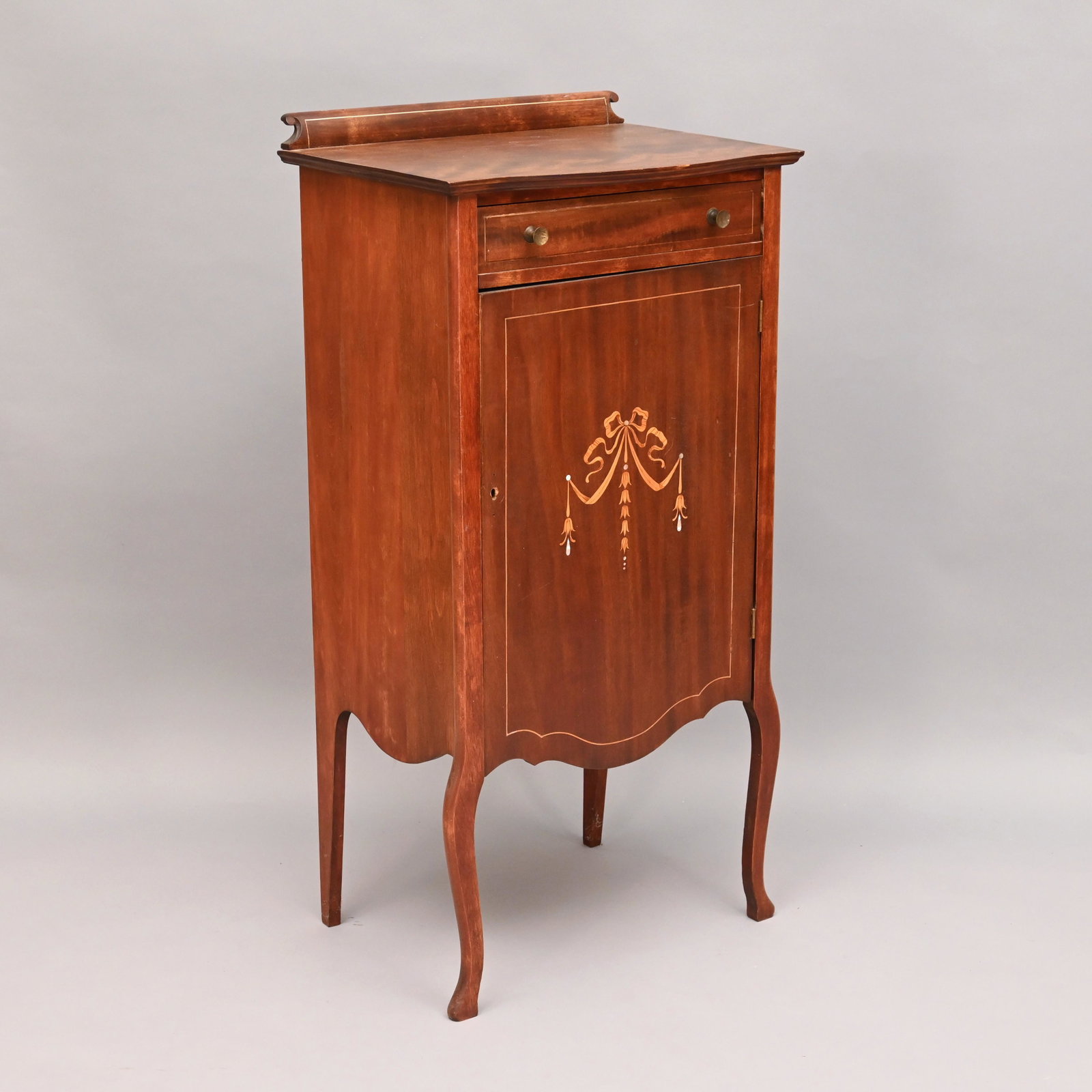 Inlaid Stained Birch Music Cabinet: The oblong top with bowed front and scrolled backsplash above a single drawer over a cabinet door opening to a fitted interior of horizontal slots, raised on cabriole legs. H: 41.5 in.; W: 20.5 in.; D