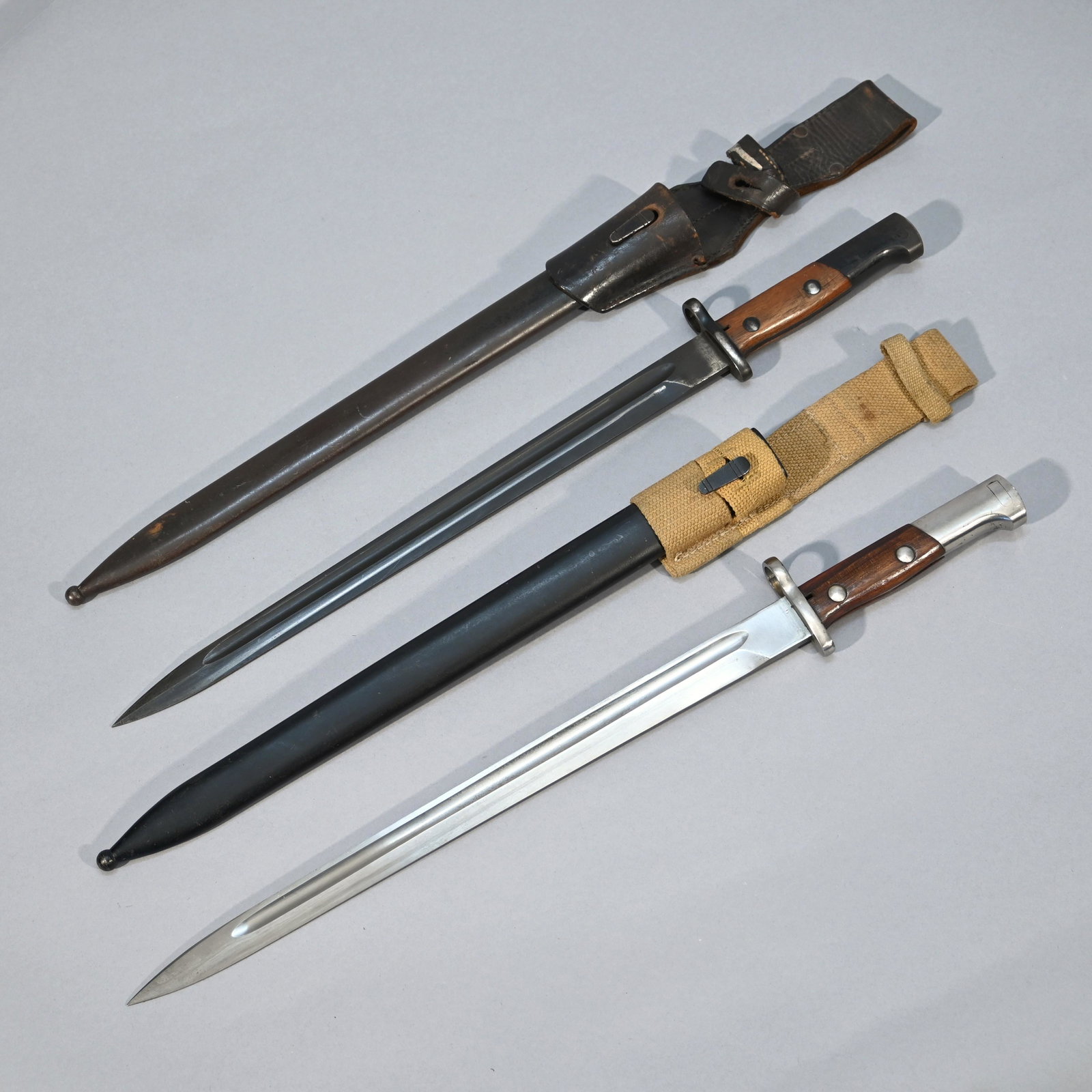 Two Belgian FN-49 Bayonets with Scabbards: Each with steel scabbards, the first with blued blade and leather frog, impressed #H2200; the second with canvas frog, impressed 7861. Blade length: 15 inches. Overall length: 20.25 inches.