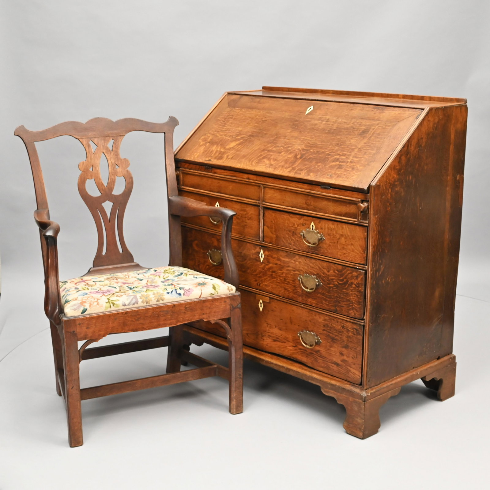 George III Oak Slant-Front Desk & Armchair: The oblong hinged top opening to a fitted stepped interior with pigeonholes, drawers and shaped valances, above a recessed panel opening to a hidden well. The case with a pair of divided panels, flank