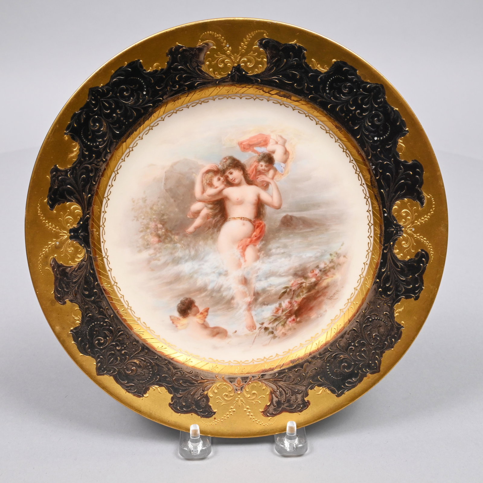 'Vienna' Porcelain 'Birth of Venus' Plate: Late Nineteenth Century. Painted with a view of 'Venus' accompanied by putti, titled on the reverse "Schaumgeboren" (Foam born"), the black and gold rim surrounded by raised foliate scrollwork panels,