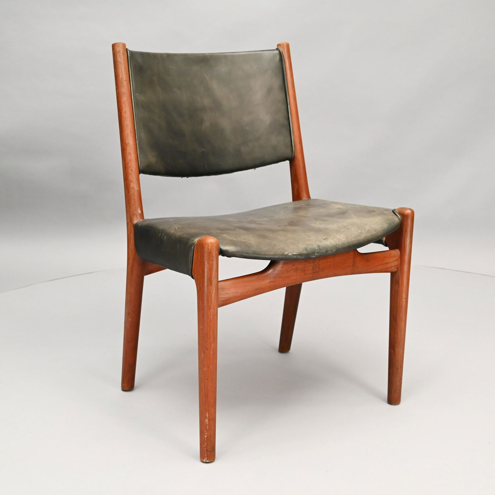Hans Wegner Teak & Leather Chair: Circa 1950, Johanes Hansen, Denmark. The black leather upholstered backrest above a conforming seat, over a shaped front seat rail, raised on rounded oblong tapered legs. H: 31 in., W: 21.25 in., D: 1