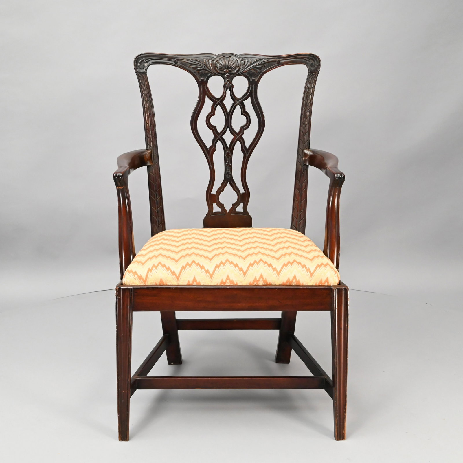 George III Carved Mahogany Armchair: The shell carved crest rail above a pierced splat, flanked by outswept arms with fluted terminals, above a trapezoidal slip seat, raised on square tapered and fluted legs, joined by a H-stretcher with