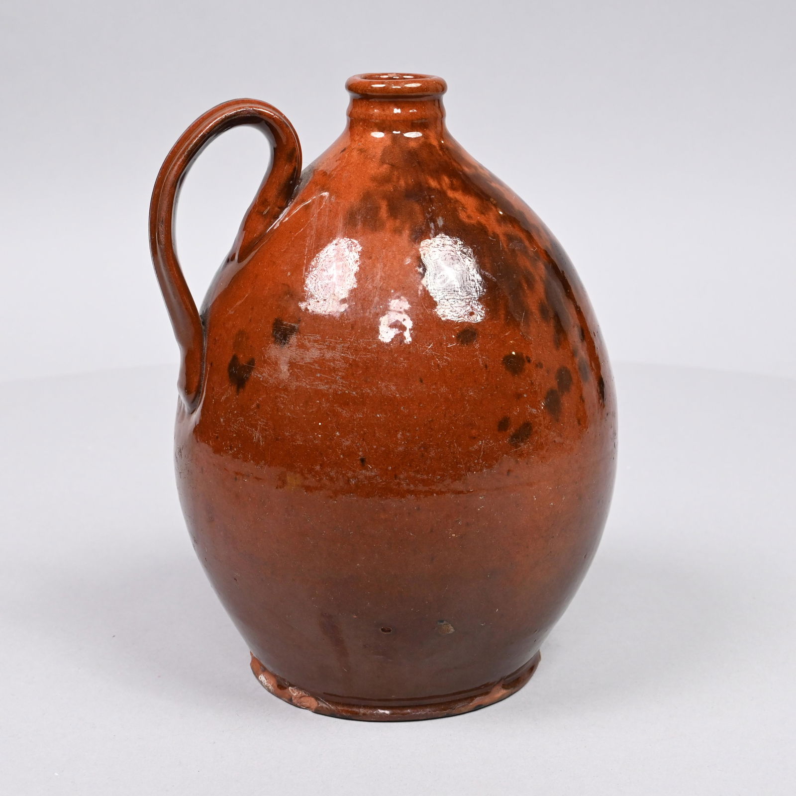 New England Redware Ovoid Jug with Manganese: The ovoid manganese splotch decorated body with applied handle, the bulbous body tapering to a rounded foot. H: 8.25 in.; Diam.: 6 in. (approx.)