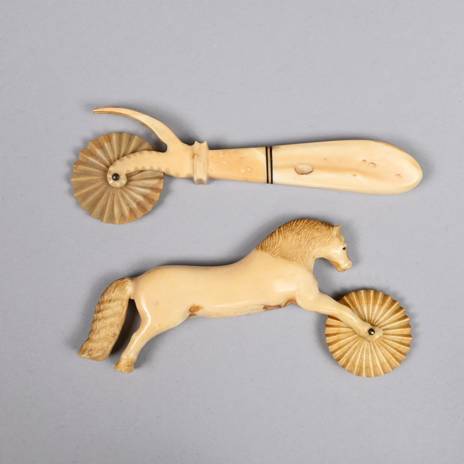 Two Sailor-Carved Whale Ivory Jagging Wheels: Both 19th century. The first figural, carved as a horse with outstretched front legs holding a fluted wheel, the mane and tail finely carved. The second with a four-tine fork (as-is) above a scrolled 