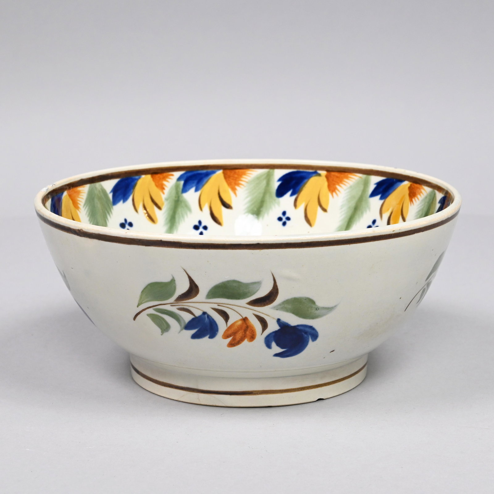 Staffordshire Pearlware Prattware Bowl, Circa 1820: Painted in Pratt colors of green, blue, orange, yellow and brown, on the interior with a floral spray, around the rim with alternating leaftips and feathery fronds, and around the exterior with leafy
